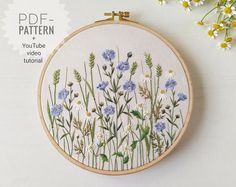 an embroidery pattern with blue and white flowers on it, next to some daisies