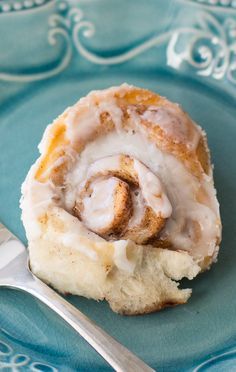 a cinnamon roll sitting on top of a blue plate next to a fork and knife