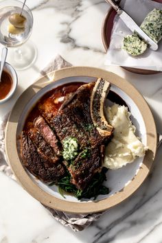 a plate with steak, mashed potatoes and sauces on it next to wine glasses