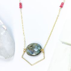 Introducing our Celestial Dreamscape Necklace, where the ethereal meets the earthly in a harmonious dance of light and color. The focal point of this enchanting piece is a large labradorite pendant, showcasing its mesmerizing play of iridescent hues. A gold-filled geometric wire artfully surrounds the labradorite, creating a unique shape that exudes celestial elegance, with intriguing negative space beneath the stone, allowing its natural beauty to breathe. The necklace is adorned with delicate Labradorite Necklace With Gemstone Accents For Gift, Mystical Oval Gemstone Necklace, Labradorite Jewelry With Gemstone Accents For Gift, Artisan Labradorite Necklace With Large Pendant, Gift Jewelry With Gemstone Accents In Labradorite, Spiritual Faceted Round Pendant Necklace, Artisan Oval Labradorite Necklace, Elegant Labradorite Oval Pendant Necklace, Labradorite Necklace With Large Pendant For Gift