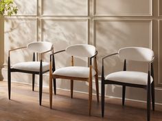 three chairs in front of a wall with wood trimming and white upholstered fabric