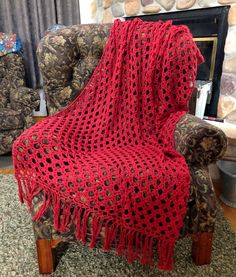 a red crocheted afghan sitting on top of a chair next to a fire place