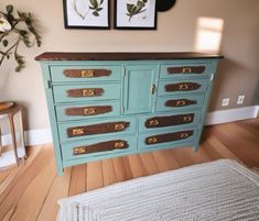 an old dresser is painted blue and has gold hardware on the drawers, along with two framed pictures above it