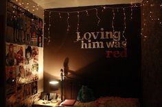 a bedroom with lights strung from the ceiling and posters on the wall above it that read loving him was red