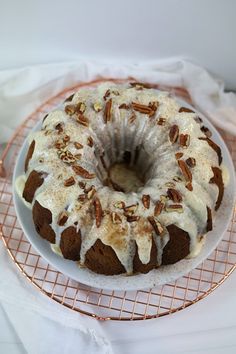 a bundt cake with white icing and nuts on a wire rack next to a napkin