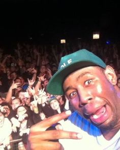 a man in a green hat is taking a selfie with his cell phone at a concert