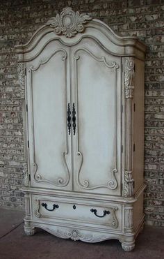 an old white armoire sitting on top of a tile floor next to a brick wall