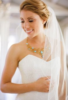 a woman in a wedding dress is smiling and looking down at her necklace on her neck