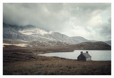 a small house sitting on top of a grass covered field next to a body of water