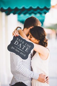 a man and woman hugging each other in front of a sign that says save the date