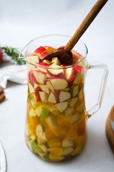 a glass pitcher filled with sliced apples on top of a white table next to other plates and utensils