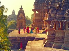 several people in red and yellow robes are walking on a path between two large stone structures