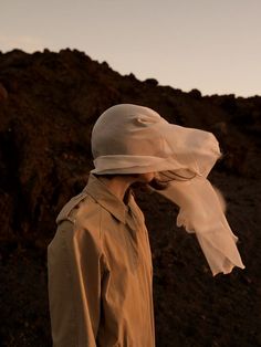 a woman wearing a white hat and trench coat standing in front of a rocky mountain