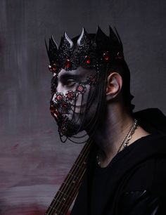 a man wearing a black mask with red eyes and horns on his head holding a guitar