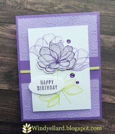 a purple and white birthday card with a flower on the front, sitting on top of a wooden table