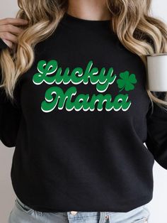 Stay warm and stylish with our Lucky Mama Women's Crewneck Sweatshirt. Featuring the words "Lucky Mama" written in a green and white retro font and a 4-leaf clover design, this sweatshirt is perfect for celebrating St. Patrick's Day or showing off your Irish heritage. Made with a high-quality Gildan Heavy Blend fabric, this sweatshirt is both durable and comfortable. Available in 3 classic colors and 6 sizes, it's perfect for any women. The crewneck design and relaxed fit make it perfect for lou Green Crew Neck Tops For St. Patrick's Day, Green T-shirt With Letter Print For Mother's Day, Mother's Day Green T-shirt With Letter Print, Green Long Sleeve Slogan T-shirt, Green Long Sleeve T-shirt With Slogan, Green Crew Neck Sweatshirt With Lettering, Green Letter Print Top For St. Patrick's Day, Green Long Sleeve Tops With Name Print, Green Long Sleeve Tops For Mother's Day