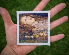 a hand is holding a small cross stitch picture