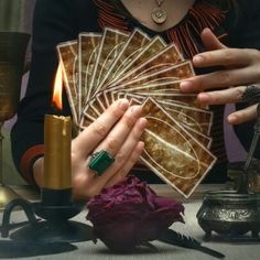 a woman sitting at a table holding up cards with candles in front of her and other items on the table