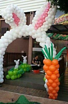 an inflatable carrot and bunny balloon arch on the side of a building with people sitting outside