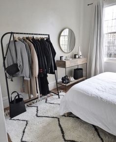 a bedroom with a bed, mirror and coat rack in the corner next to a window