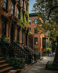 an alleyway with many brownstone buildings and trees on both sides, people walking down the street