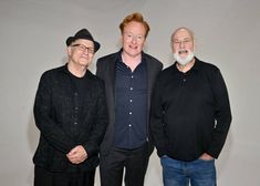 three men standing next to each other in front of a white wall