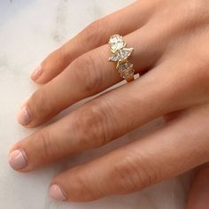 a woman's hand wearing a gold ring with two diamonds on it and one diamond in the middle