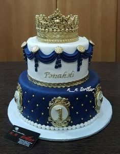 a three tiered cake decorated with blue and white frosting, gold trimmings and a crown on top