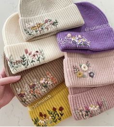 a hand is holding five beanies with flowers on them