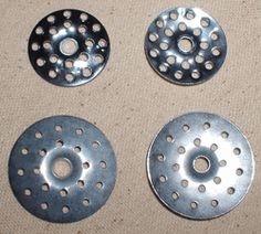 four metal discs with holes in them sitting on a table next to a brown cloth