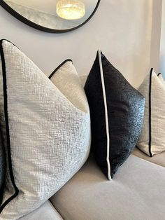 three black and white pillows sitting on top of a couch next to a round mirror