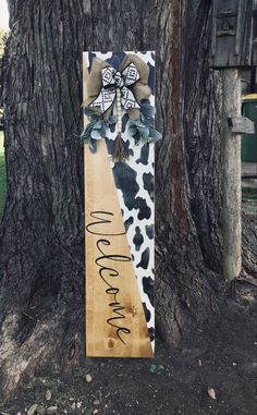 a wooden sign that reads welcome home next to a tree with a cow print bow on it