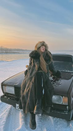 a woman sitting on the hood of a car in the snow