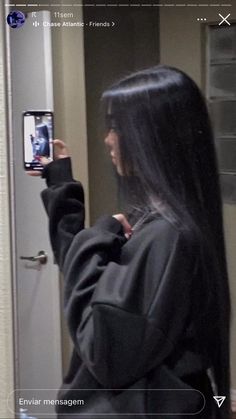 a woman taking a selfie with her cell phone in front of the door while wearing a black hoodie