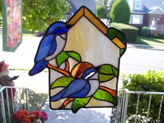 a stained glass birdhouse hanging from a tree with green leaves and blue birds on it