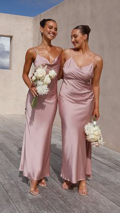 two women standing next to each other on a wooden deck holding bouquets and flowers