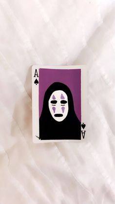 a playing card with a face painted on the front and purple back, sitting on a white sheet