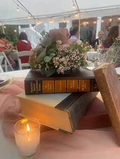 a stack of books sitting on top of a table next to a candle and flowers