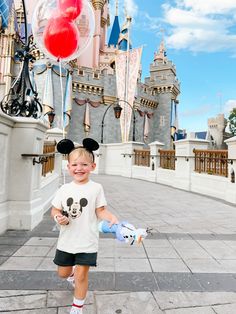 a little boy that is standing in front of a castle with mickey mouse ears on