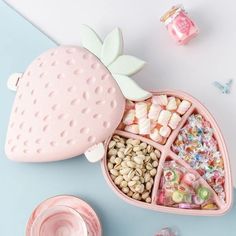 a pink heart shaped container filled with candy and candies next to other sweets on a blue surface