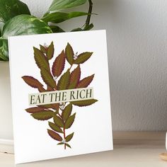 a card with the words eat the rich on it next to a potted plant