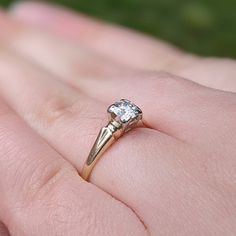 a close up of a person's hand holding a ring with a diamond on it