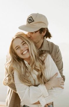 a man and woman hugging each other while standing next to each other in front of the ocean