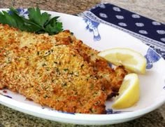 two pieces of fish on a plate with lemon wedges and parmesan cheese