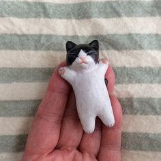 a small black and white cat figurine held in someone's hand on a striped blanket