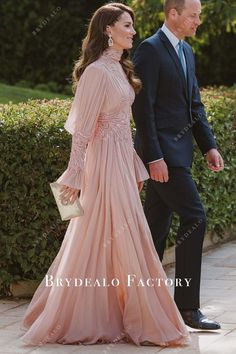 a woman in a long pink dress walking next to a man in a suit and tie