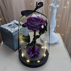 a purple rose in a glass dome with fairy lights on the side and a black box behind it