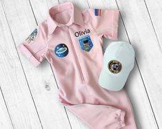 a pink nasa suit and cap laying on top of a white wooden floor next to a baseball cap