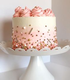 a pink and white cake with gold sprinkles on it sitting on a plate