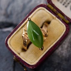 a ring with a green leaf on it sitting in a red velvet case next to a card